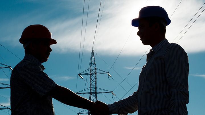 Dos hombres se dan la mano delante de cables eléctricos.