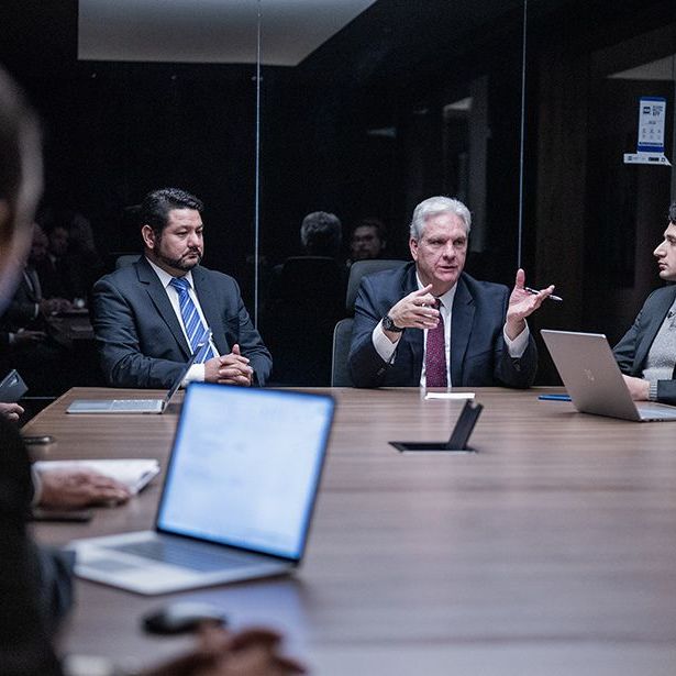 A group of people are sitting around a conference table with laptops