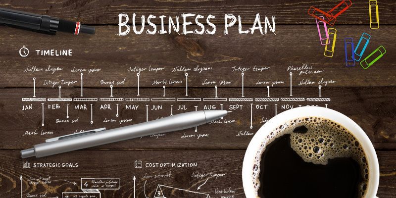 A cup of coffee is sitting on a wooden table next to a business plan.