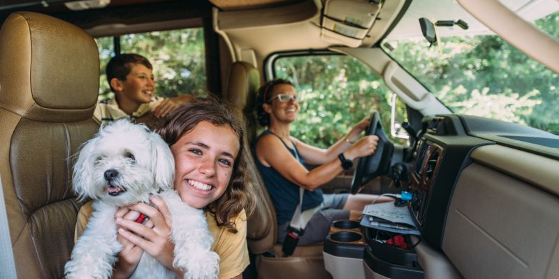 A family is sitting in the back seat of a car holding a dog.