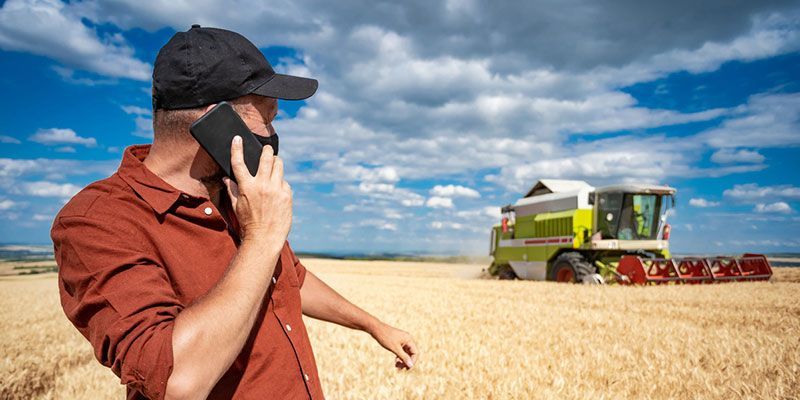 A man is talking on a cell phone in a field with a combine harvester in the background.