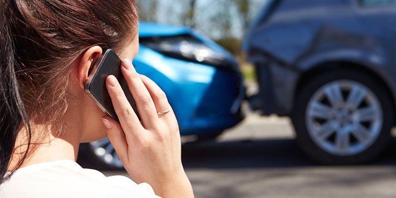 A woman is talking on a cell phone in front of a car accident.