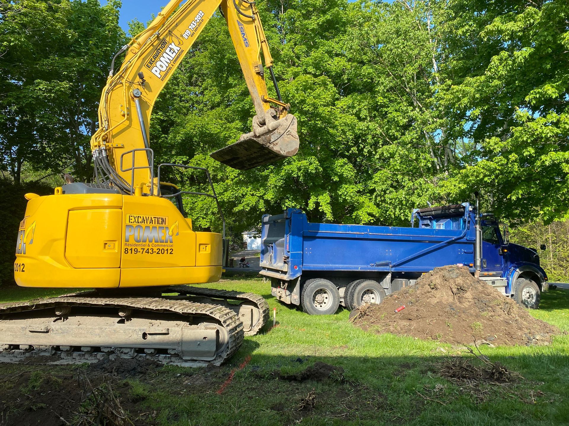 Une excavatrice jaune charge de la terre dans un camion-benne bleu.