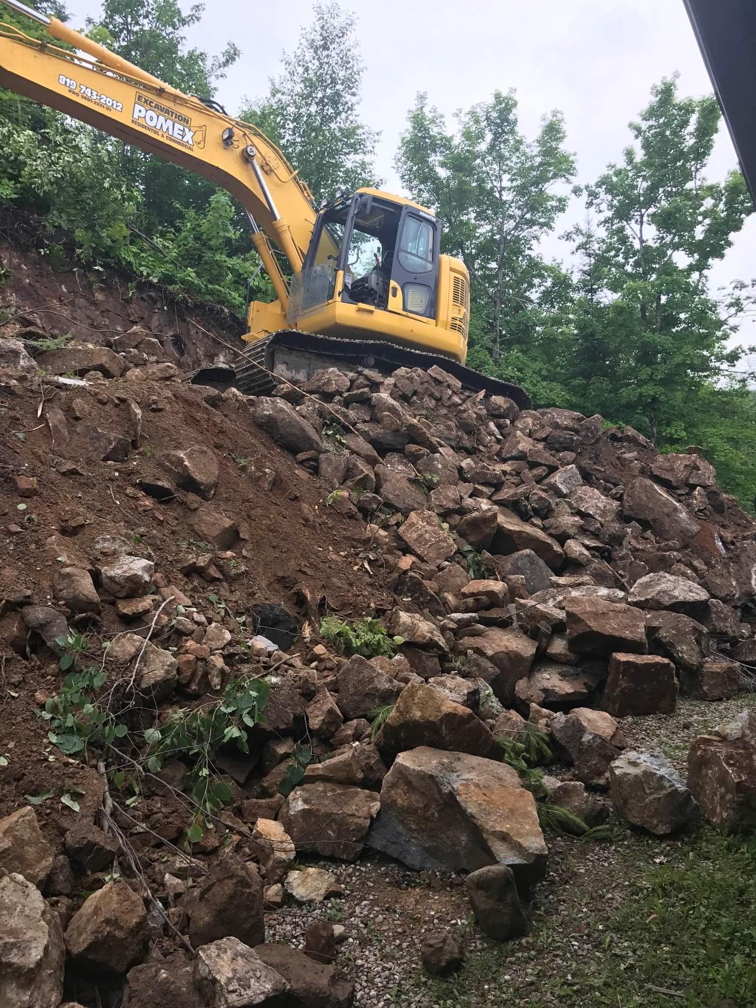 A yellow excavator is working on a pile of rocks.