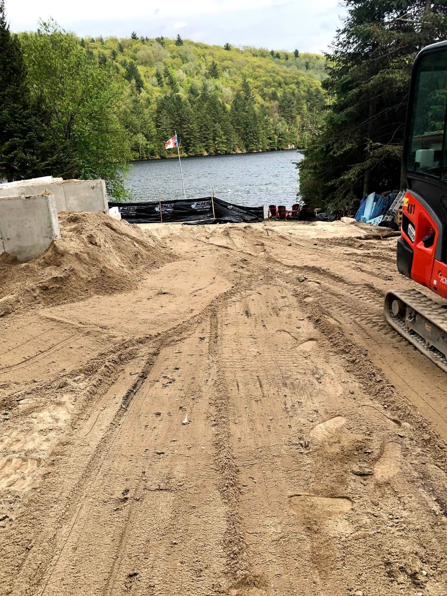 Un bulldozer roule sur un chemin de terre à côté d'un lac.