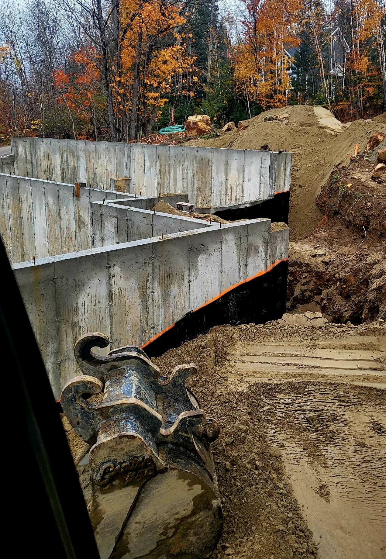 Un grand mur de béton est en cours de construction à côté d'un gros tas de terre.