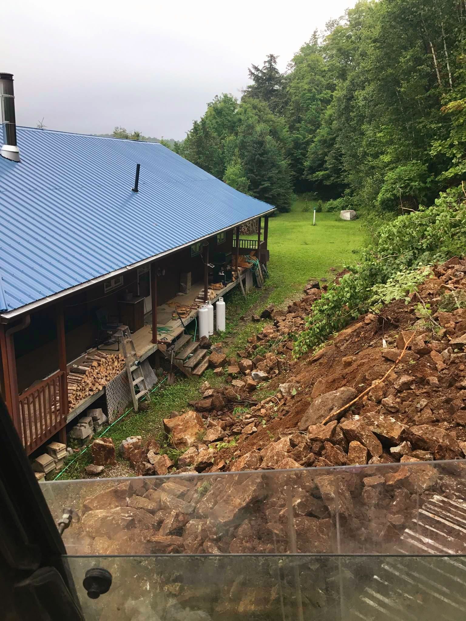 Une maison avec un toit bleu et un gros tas de terre devant.