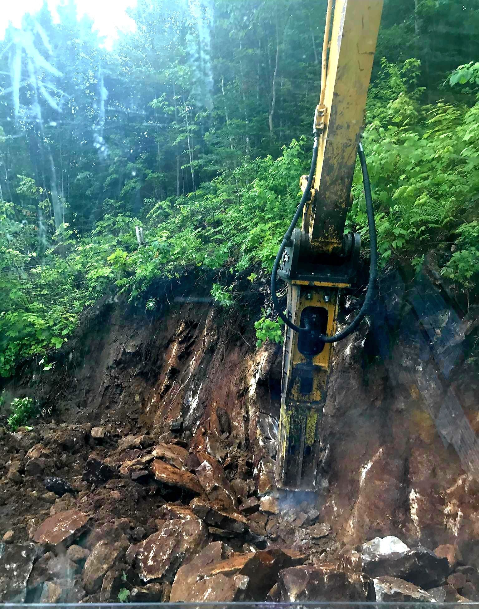 A yellow excavator is working on a pile of rocks in the woods.