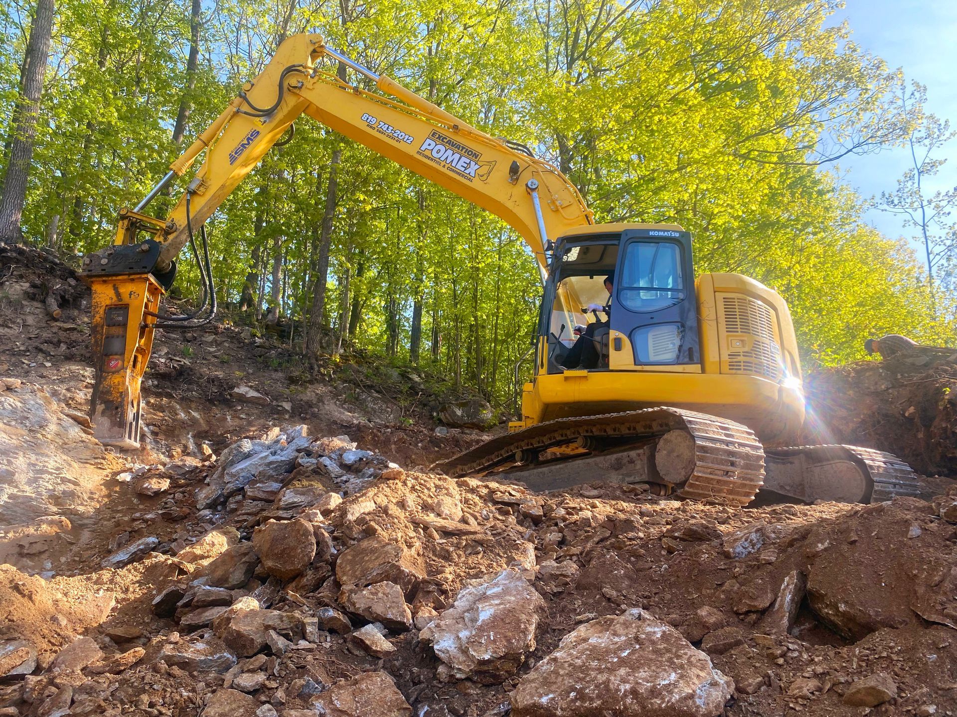 Une excavatrice jaune travaille sur un tas de rochers dans les bois.