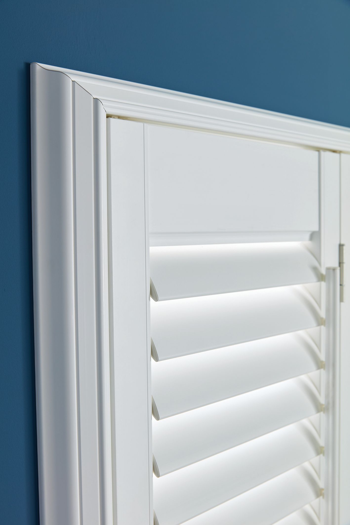 A close up of a white window shutter on a blue wall.