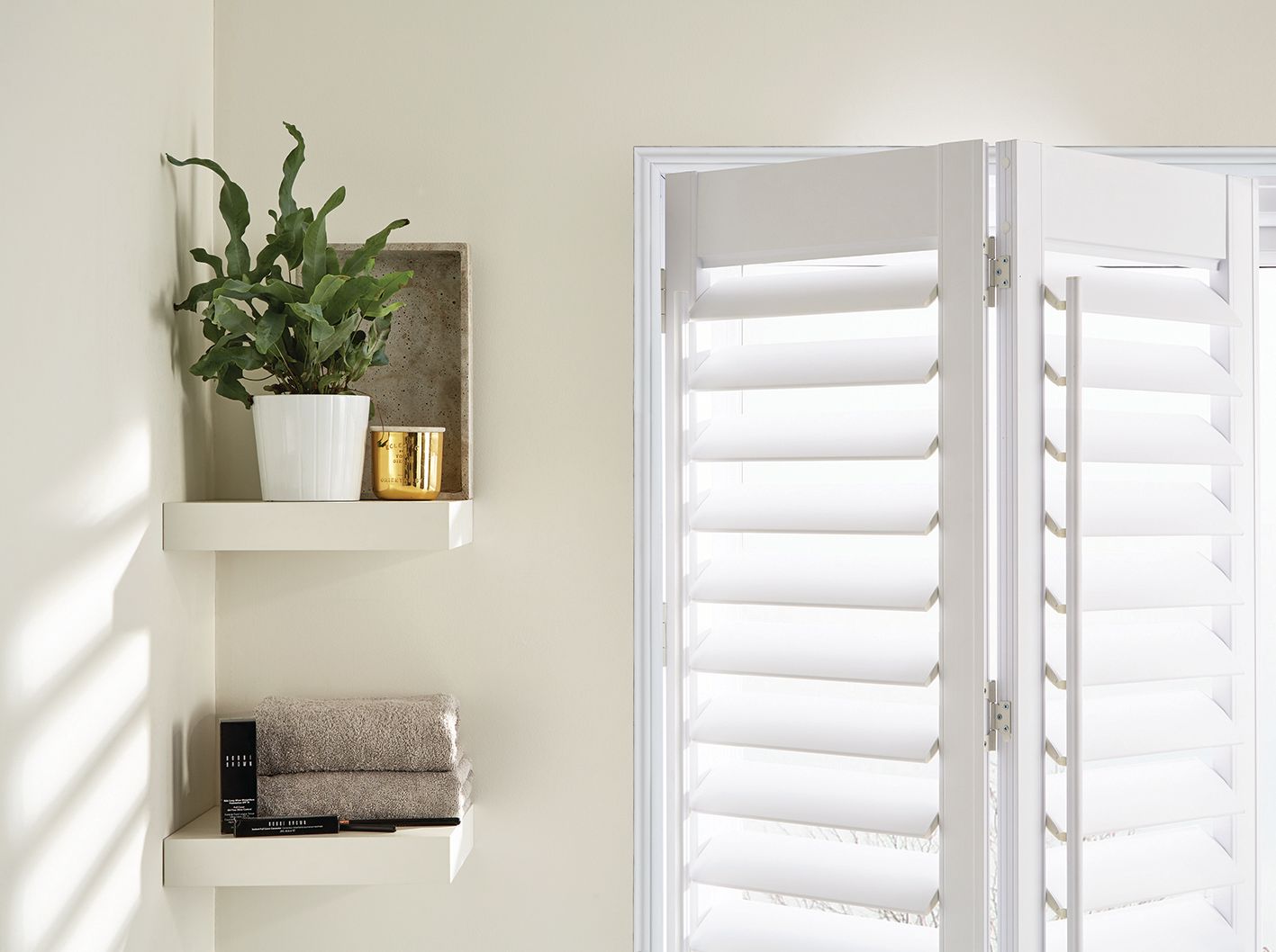 A bathroom with white shutters and a plant on a shelf.