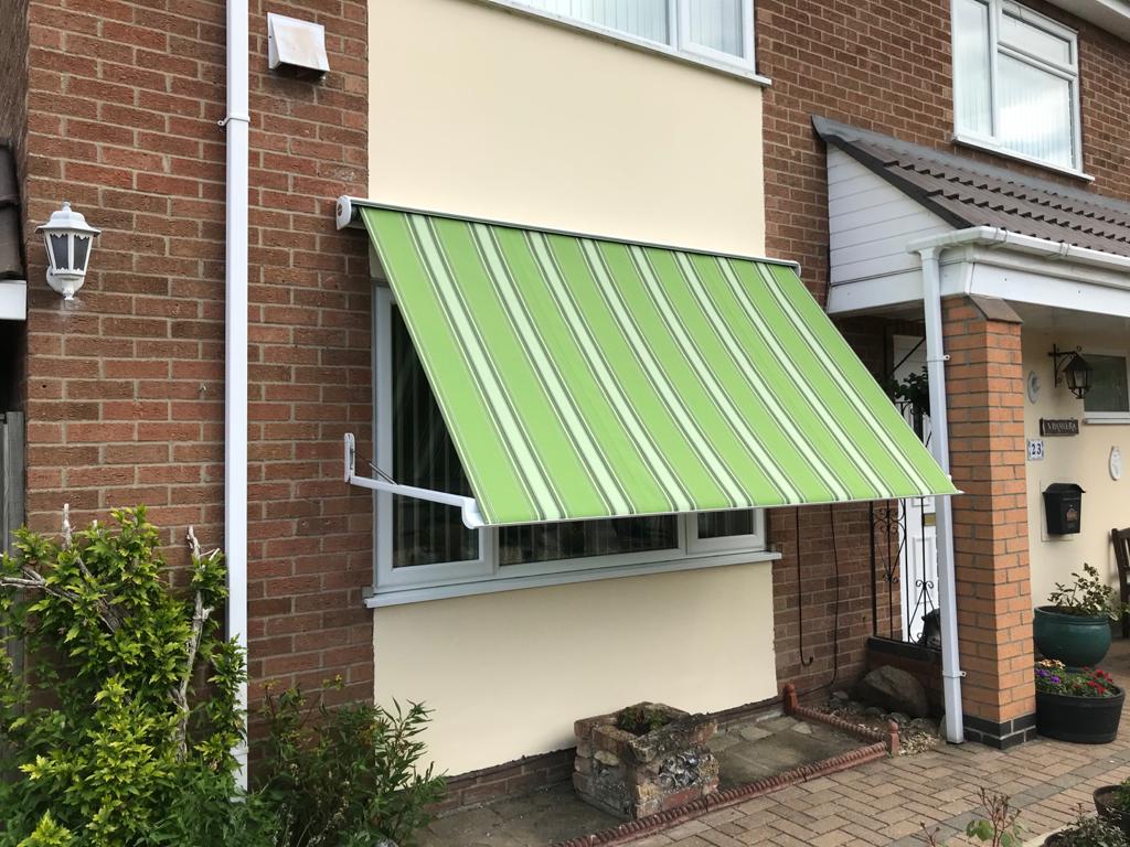 A green awning is hanging over a window on the side of a house.