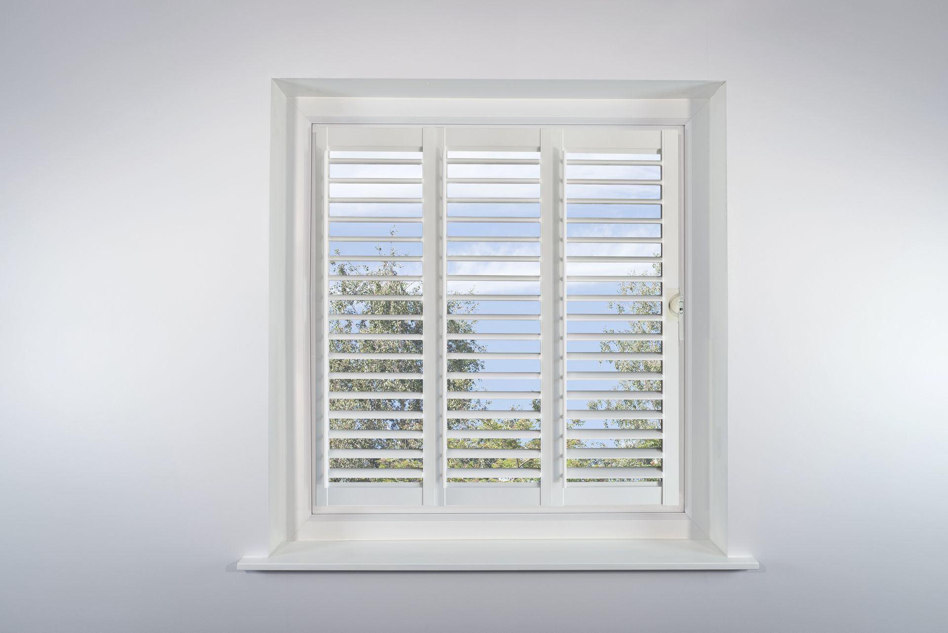 A window with white shutters on it is against a white wall.