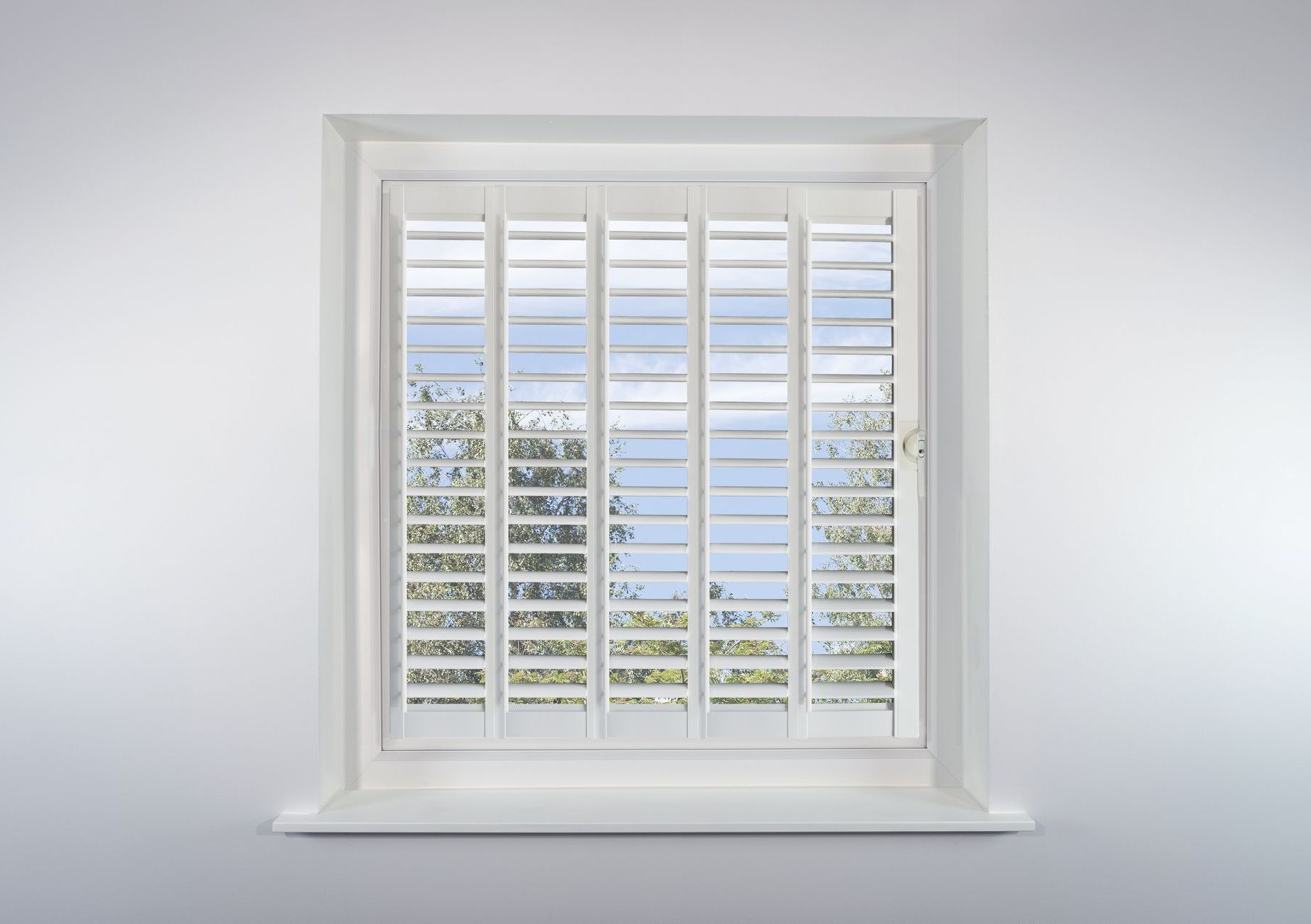 A window with white shutters on it is against a white wall.