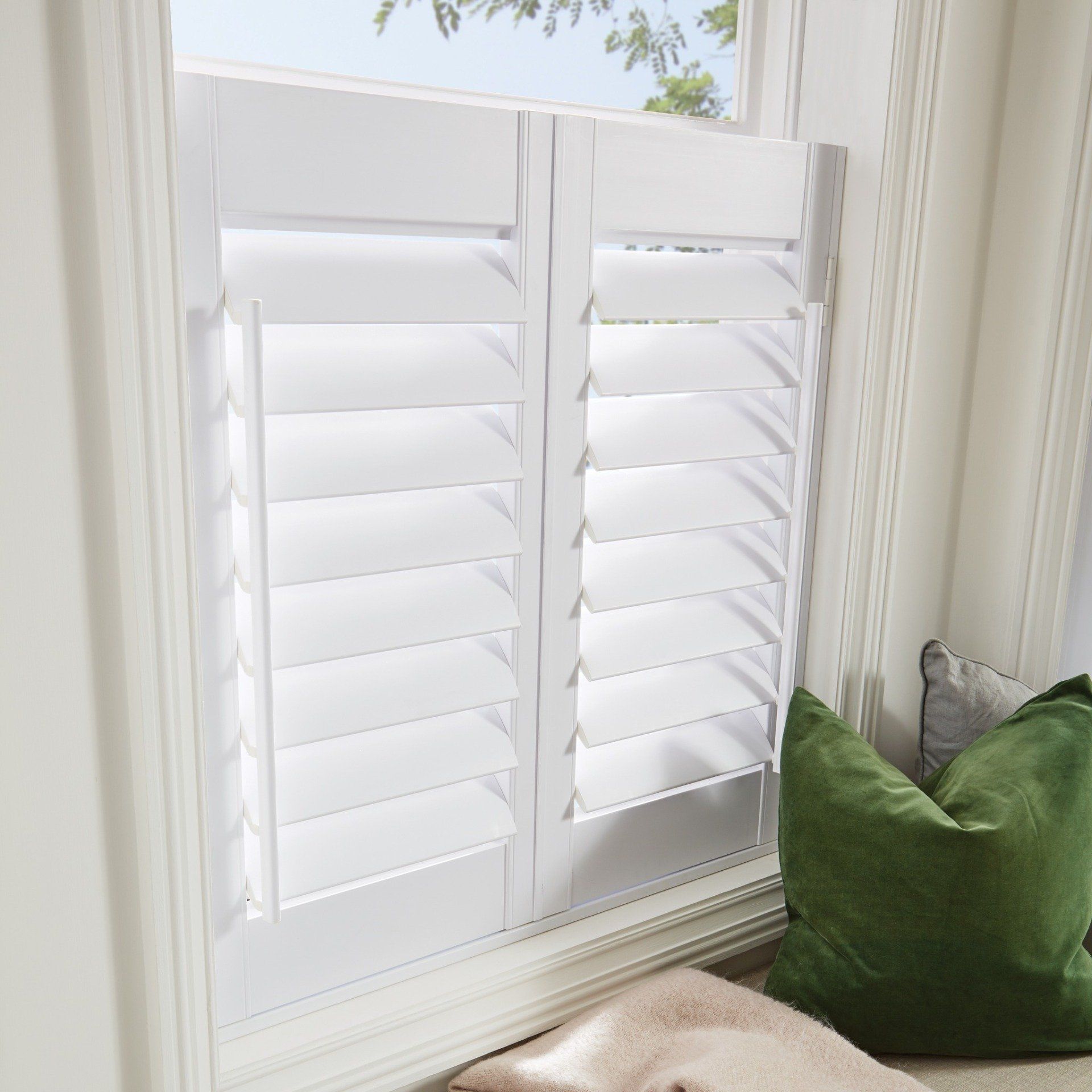 A window with white shutters and a green pillow in a living room.