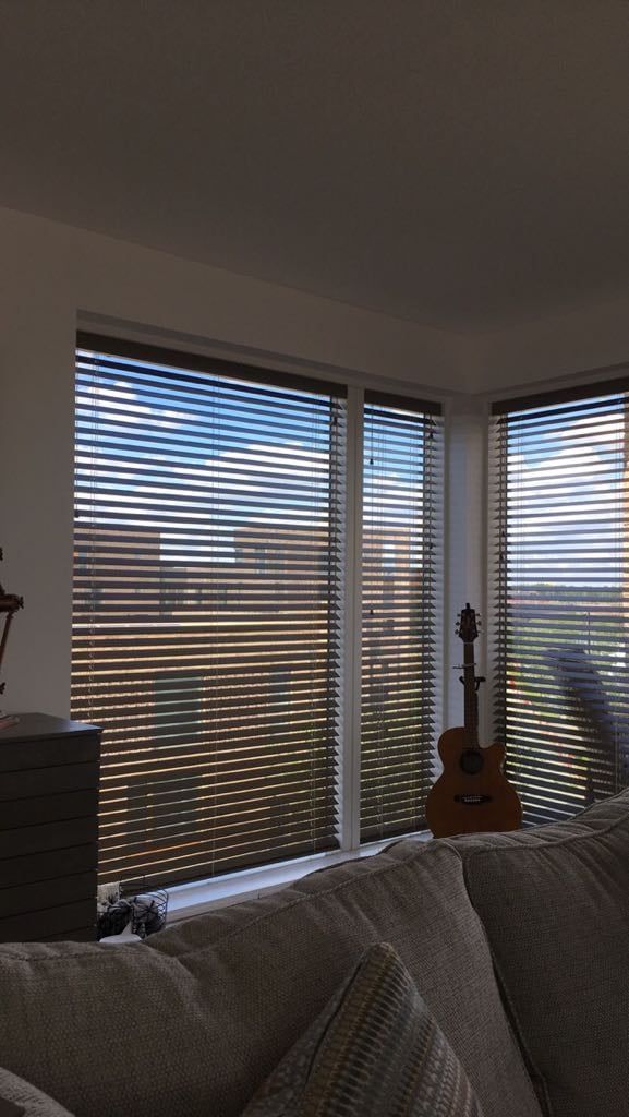 A living room with a couch and a guitar in front of a window with blinds.