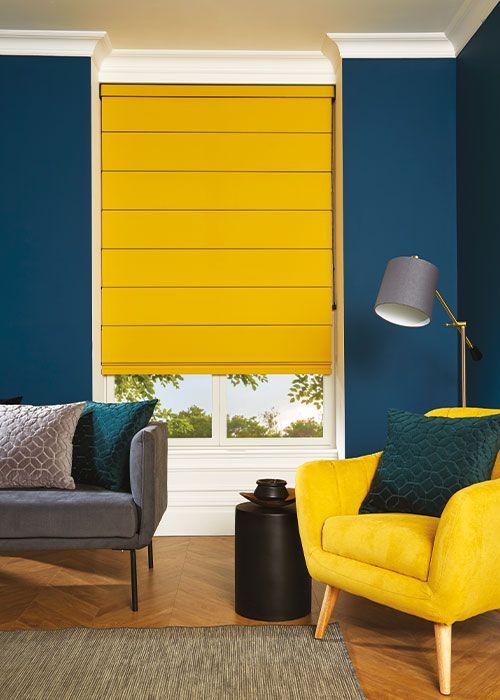 A living room with a couch , chair , lamp and yellow blinds.