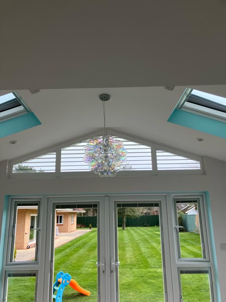 A view of a lush green yard through a window with a chandelier hanging from the ceiling.