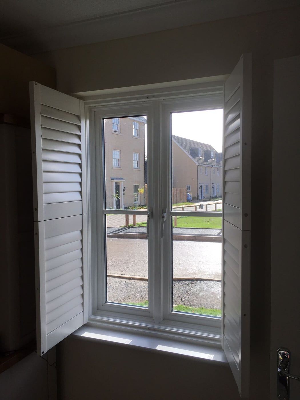 A window with shutters open and a view of a building.