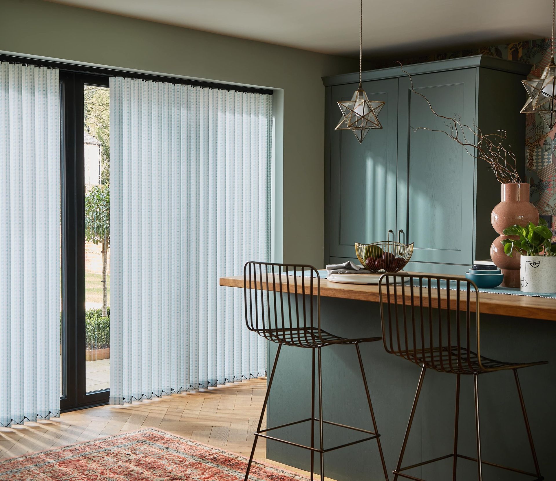 A kitchen with a bar and stools and vertical blinds on the windows.