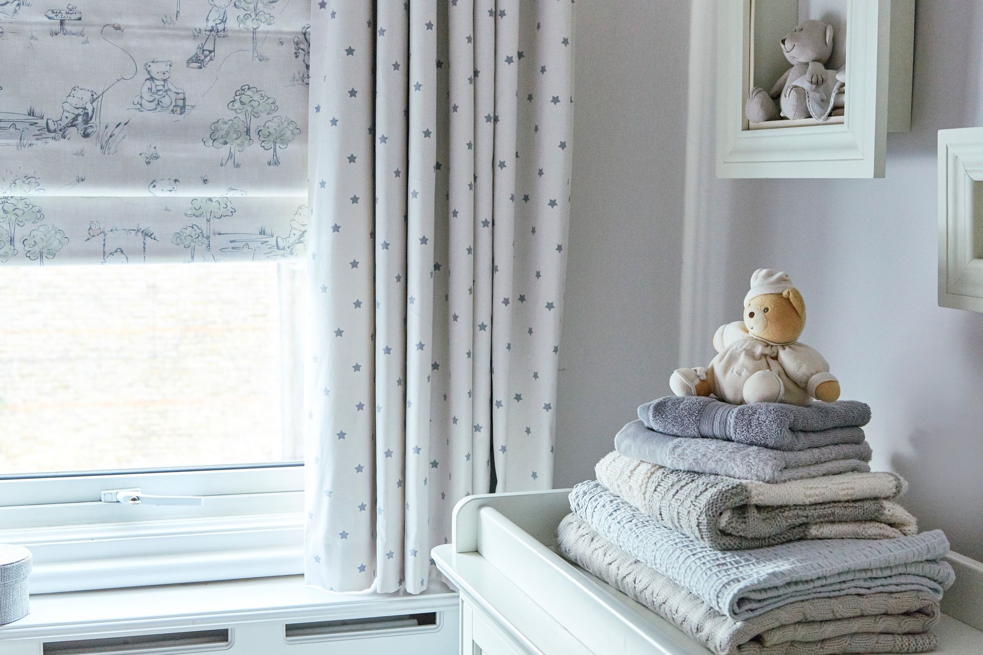 A teddy bear is sitting on top of a stack of towels in a room.