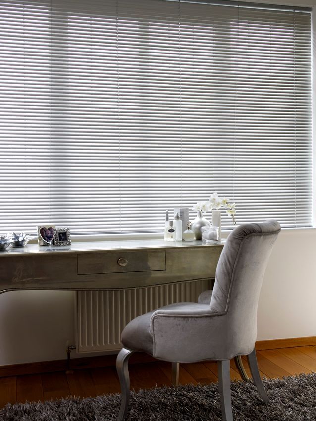 A chair is sitting in front of a desk in a room with blinds on the window.
