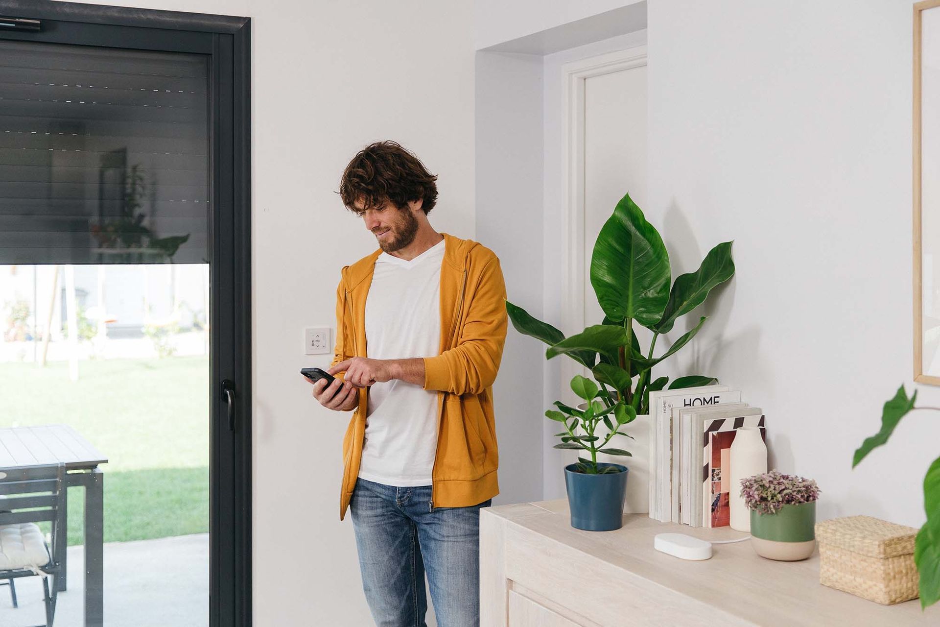 A man is standing in a living room looking at his cell phone.