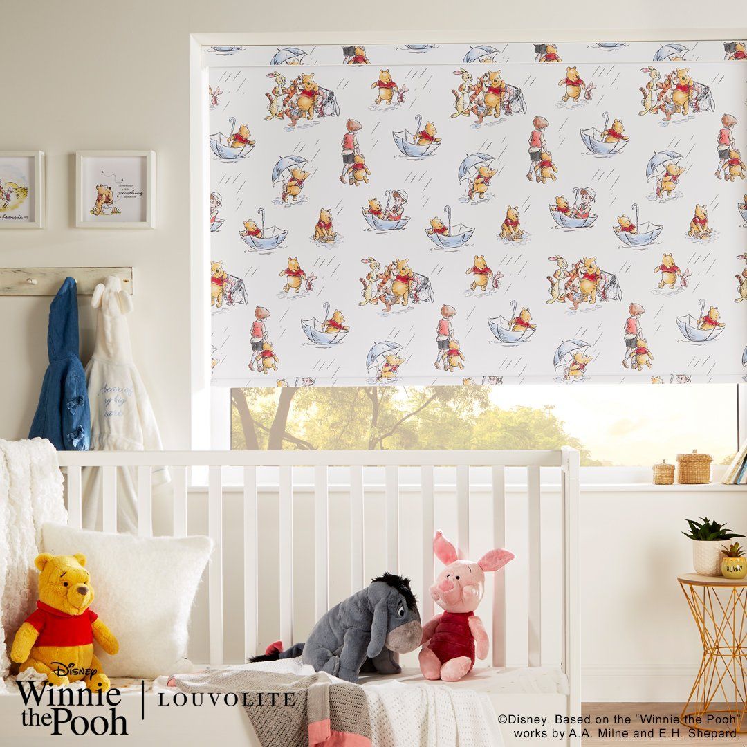 A room with a crib , a window , and a winnie the pooh blind.