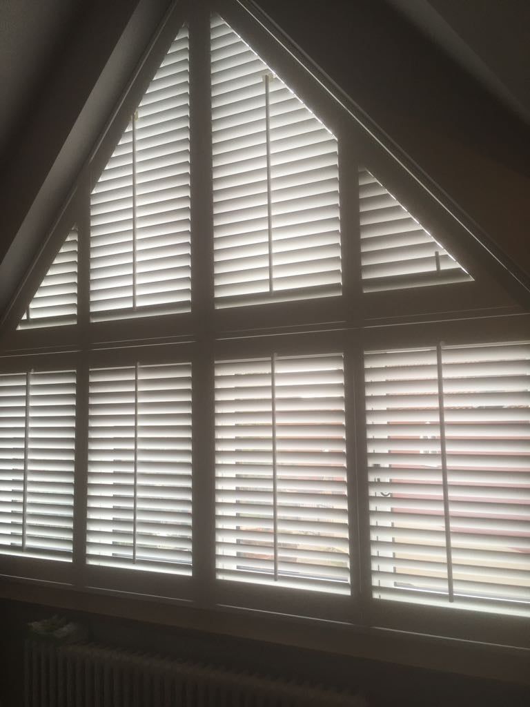 A triangle shaped window with white blinds on it