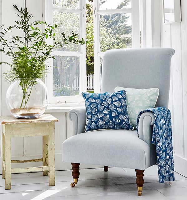 A chair with blue and white pillows sits in front of a window