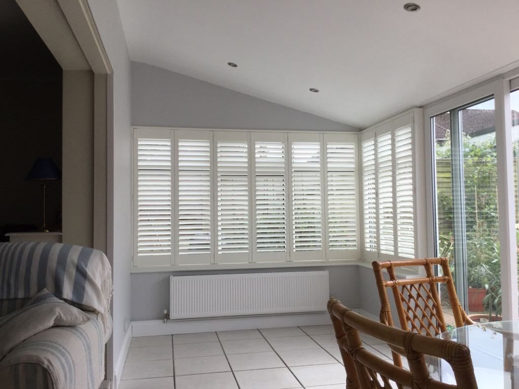 A living room with white shutters on the windows and a dining table and chairs.