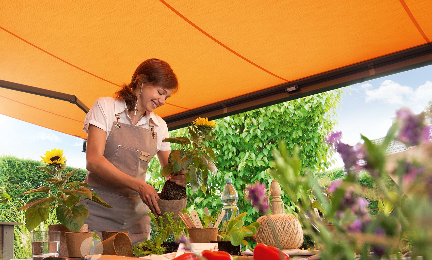 A woman is watering plants under an awning on a patio.