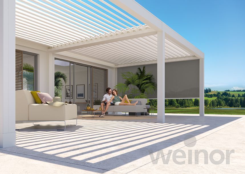 A couple is sitting on a couch under a pergola.