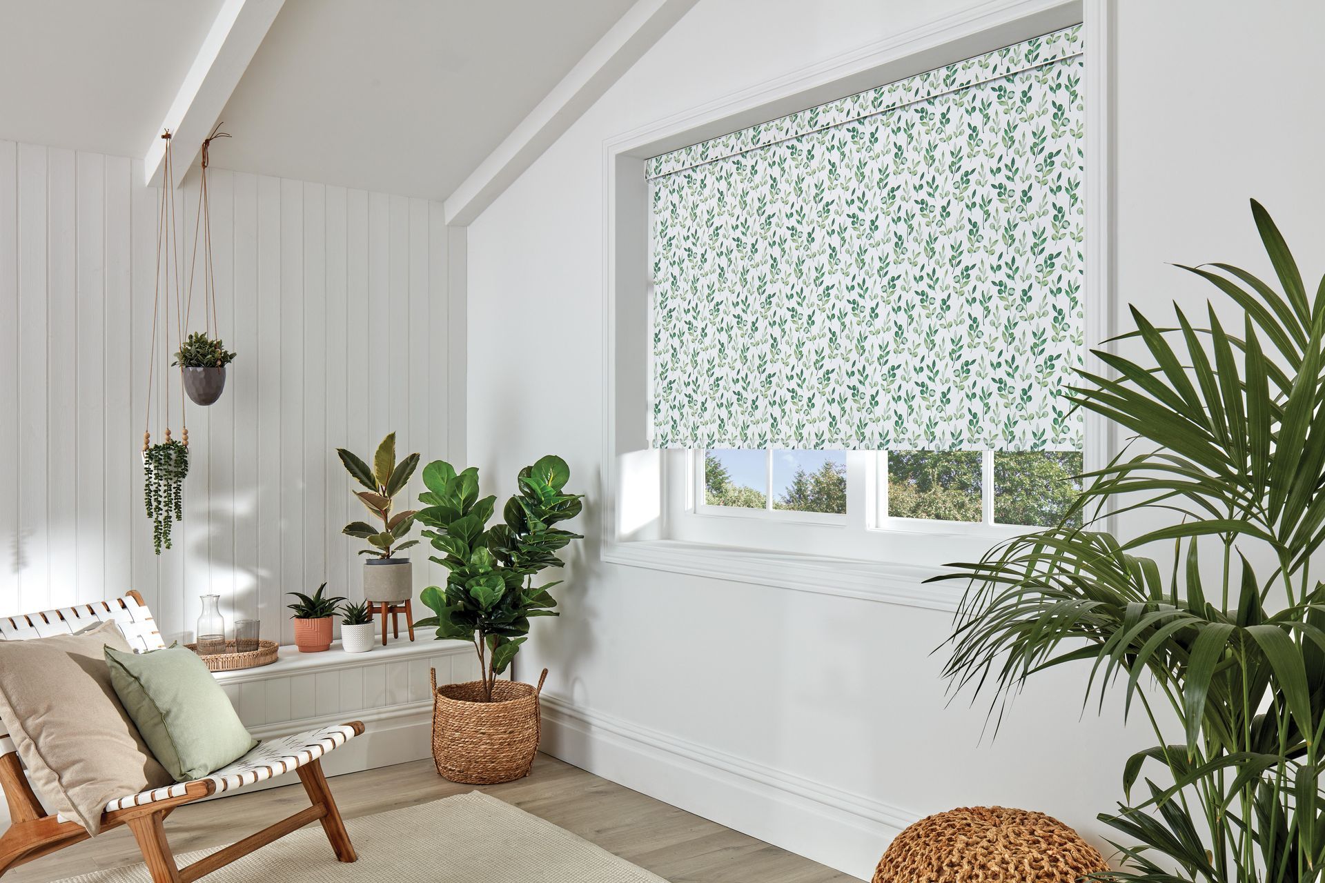 A living room with a couch , chair , potted plants and a window.