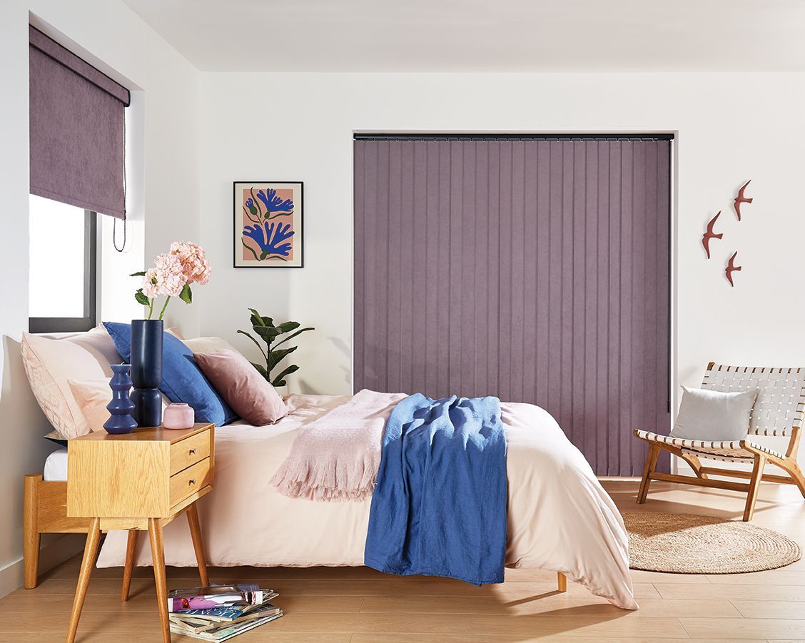 A bedroom with a bed , nightstand , chair and purple vertical blinds.