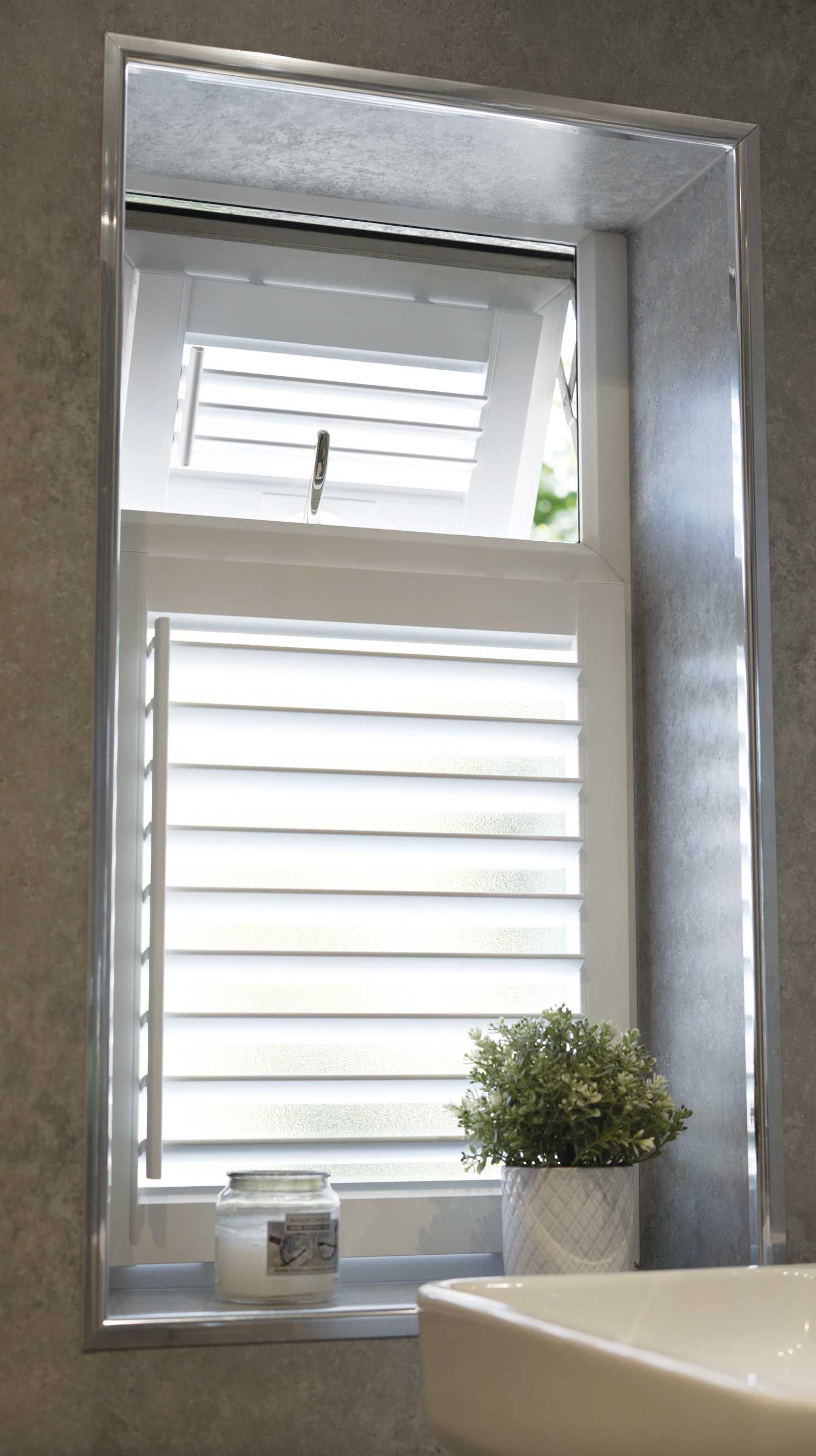 A bathroom window with white shutters and a potted plant on the window sill.