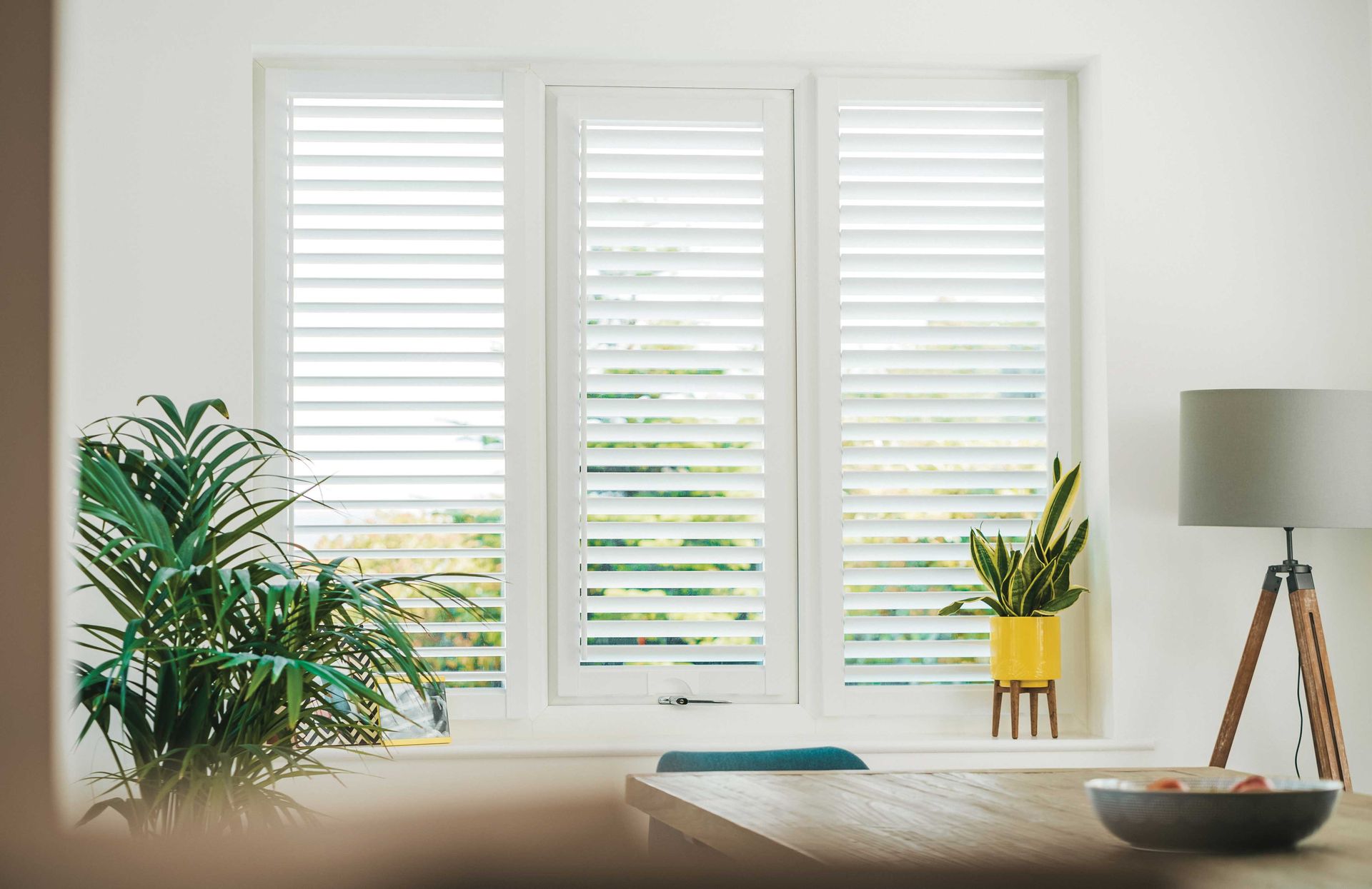 A living room with a table and a window with white shutters.