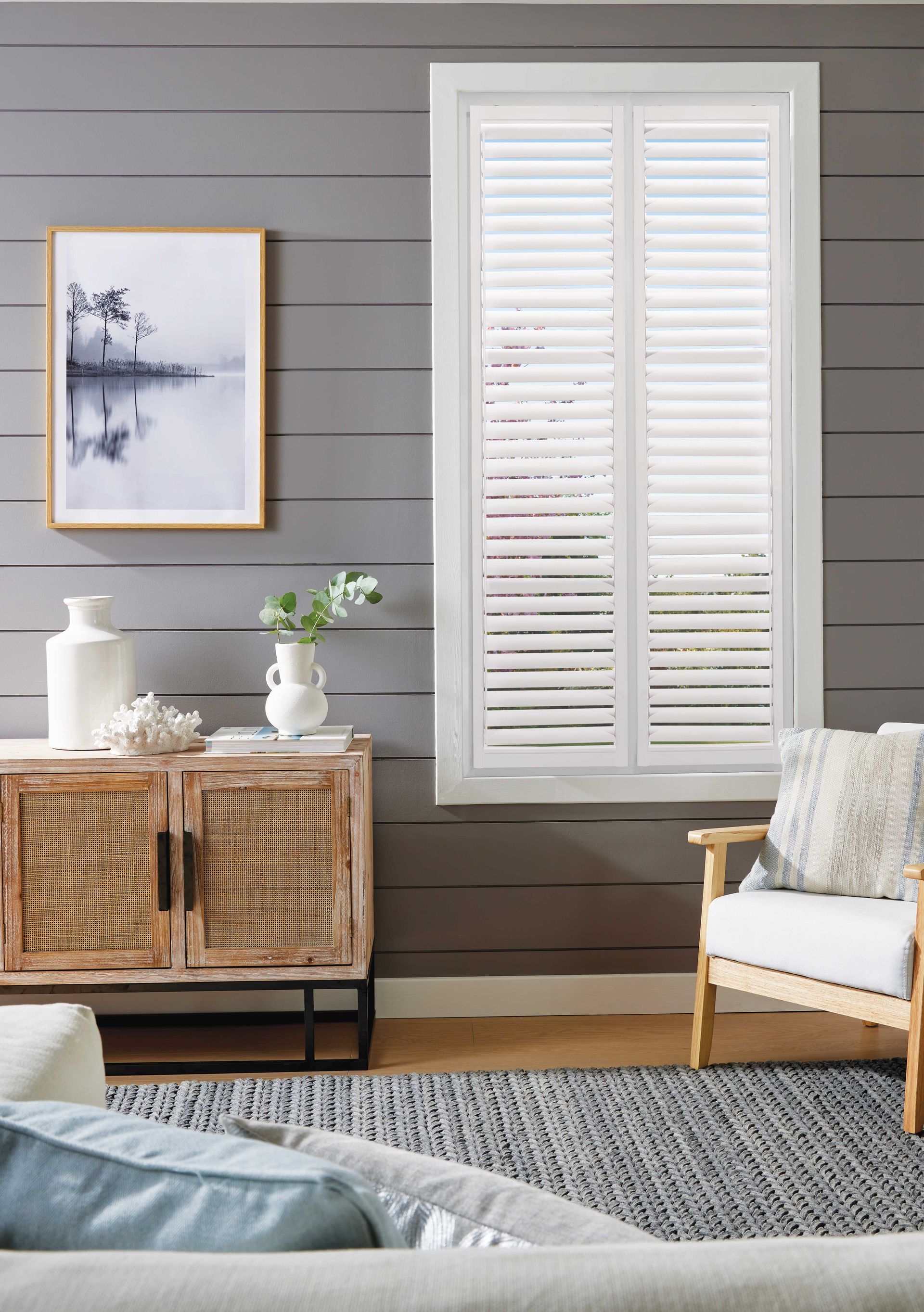 A living room with a couch , chair , table and window with white shutters.