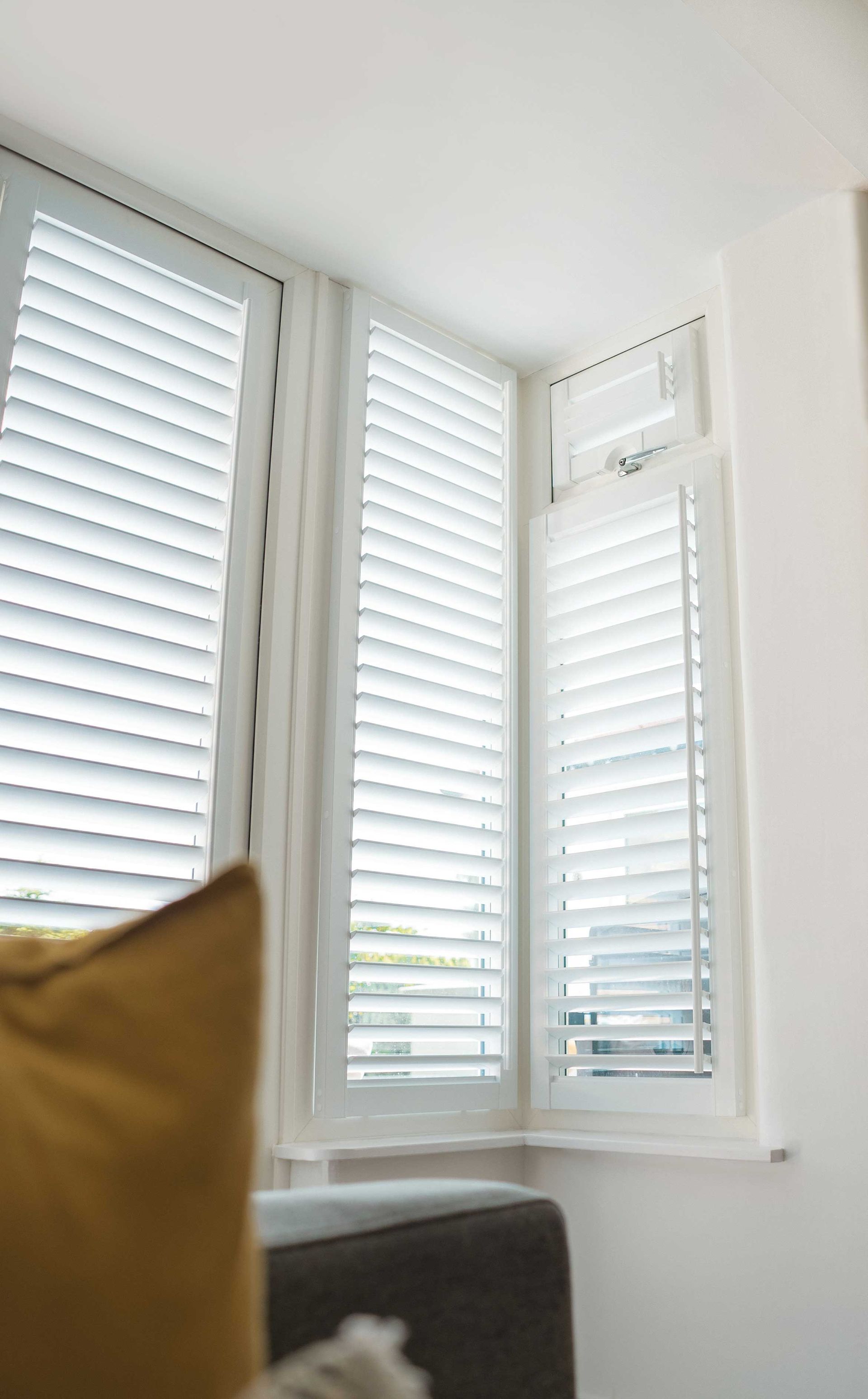 A living room with a couch and a window with white shutters.