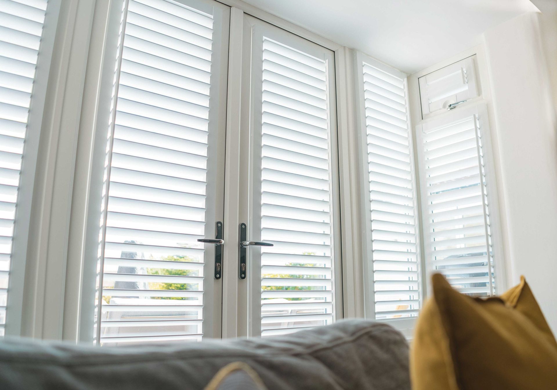 A living room with white shutters on the windows and a couch.