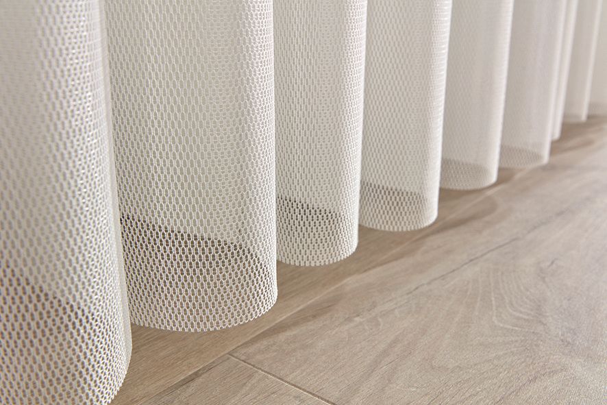 A close up of a row of white curtains on a wooden floor.