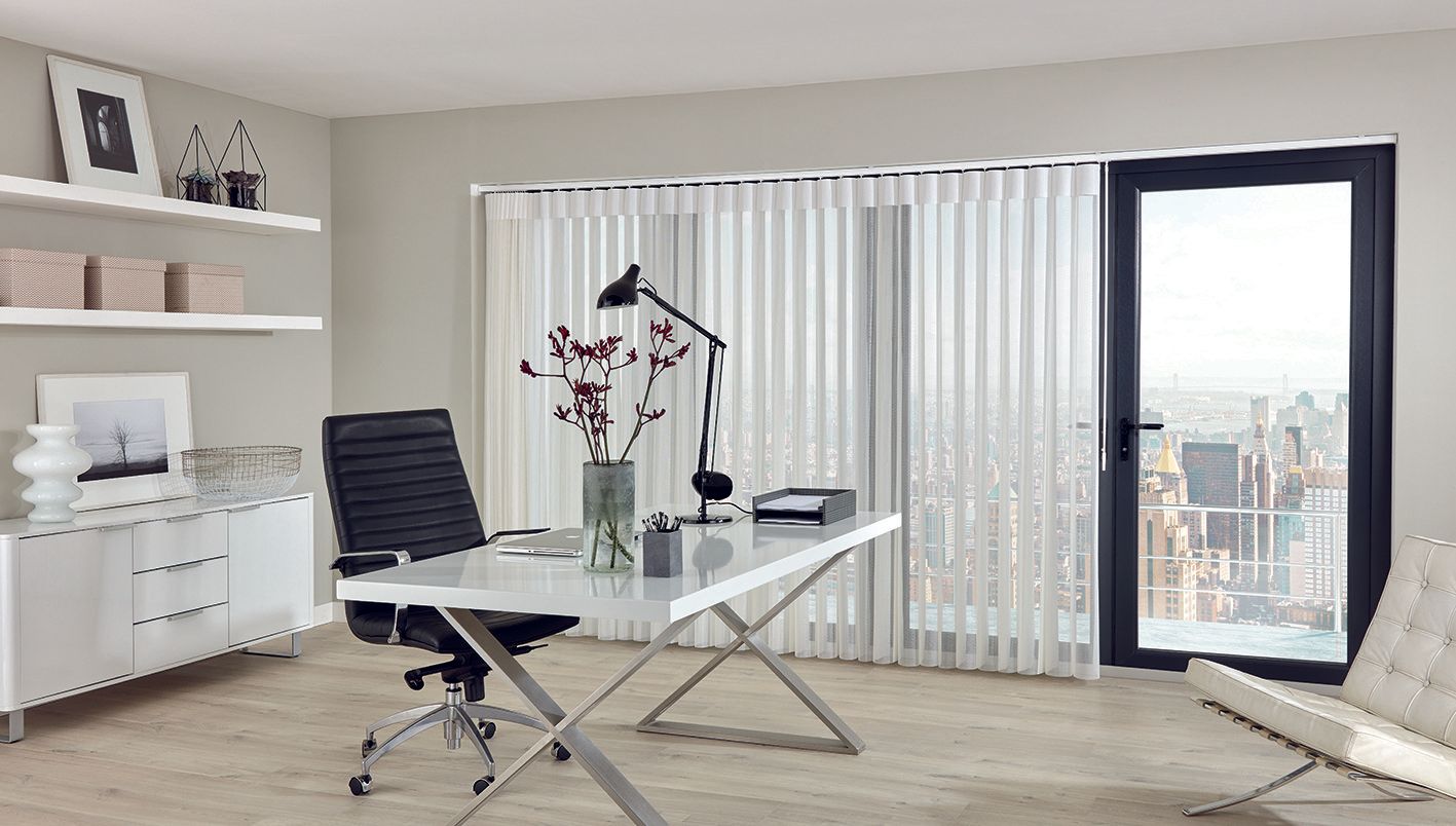 A home office with a desk , chair , lamp and sliding glass door.