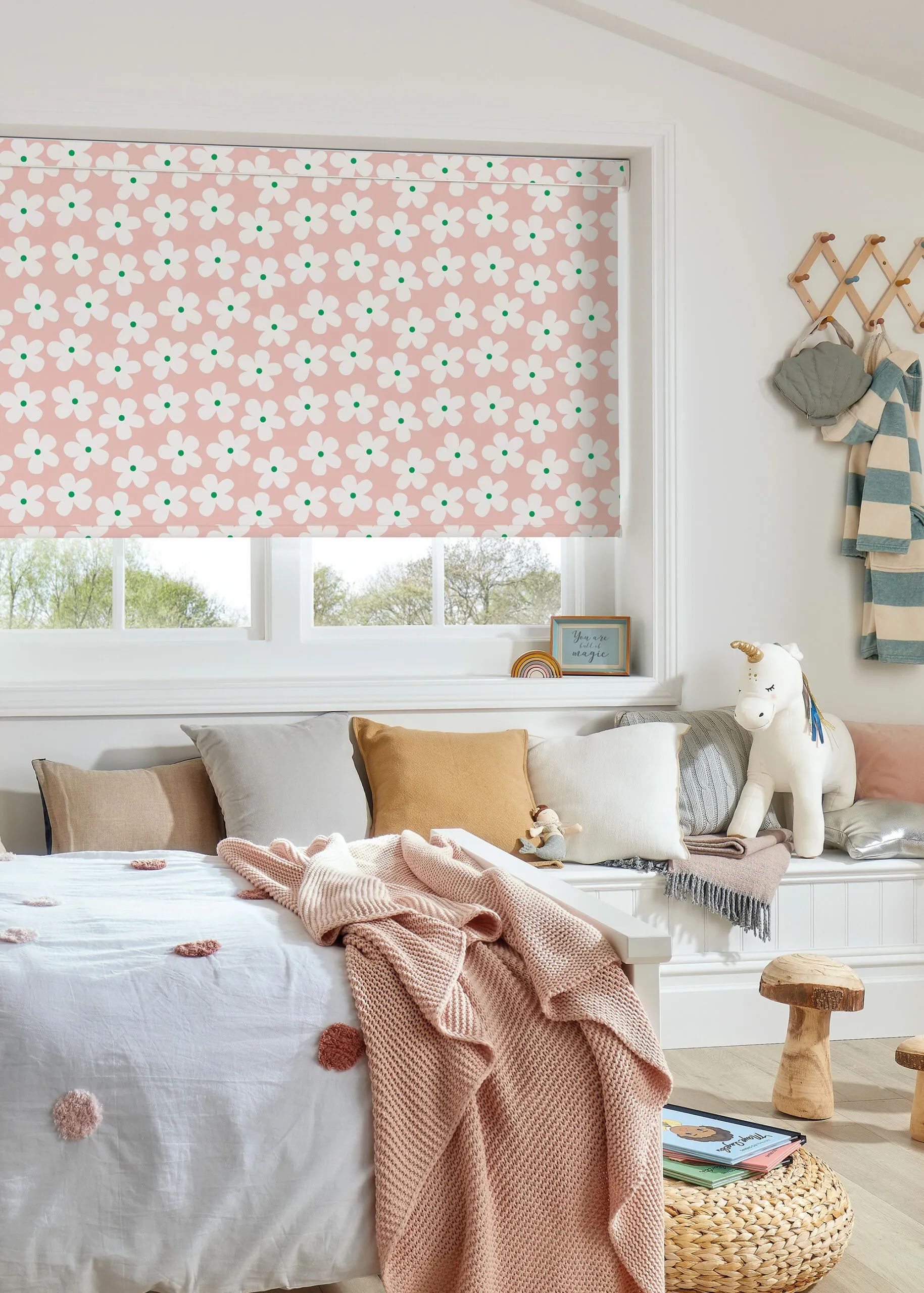 Pink floral patterned window shade in a child's bedroom with pillows and a blanket.