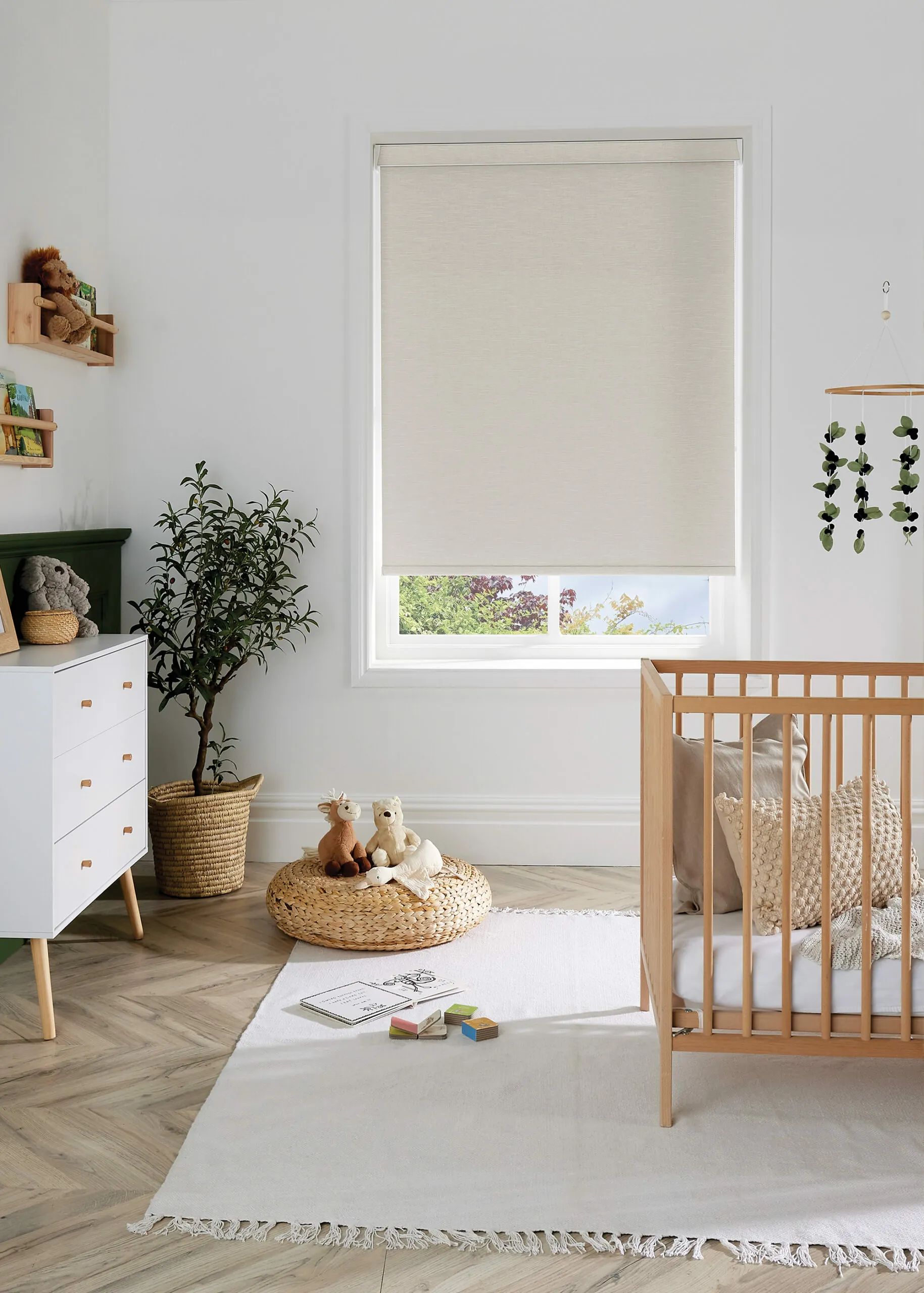 Cozy nursery with a crib, chest of drawers, and closed window blinds. A white rug and woven basket are in front of the crib.