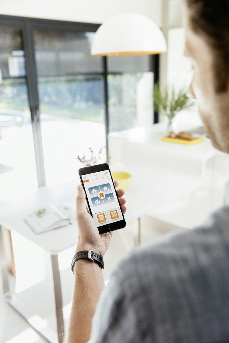 A man is holding a cell phone in his hand in front of a window.