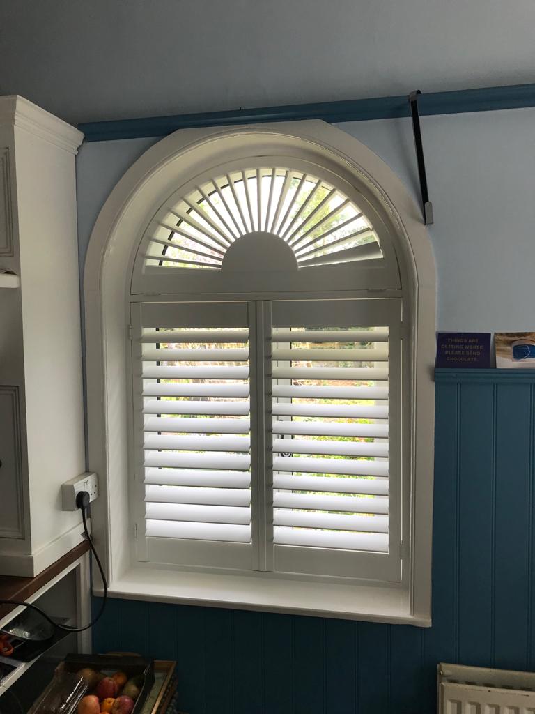 A kitchen window with arched shutters on it.