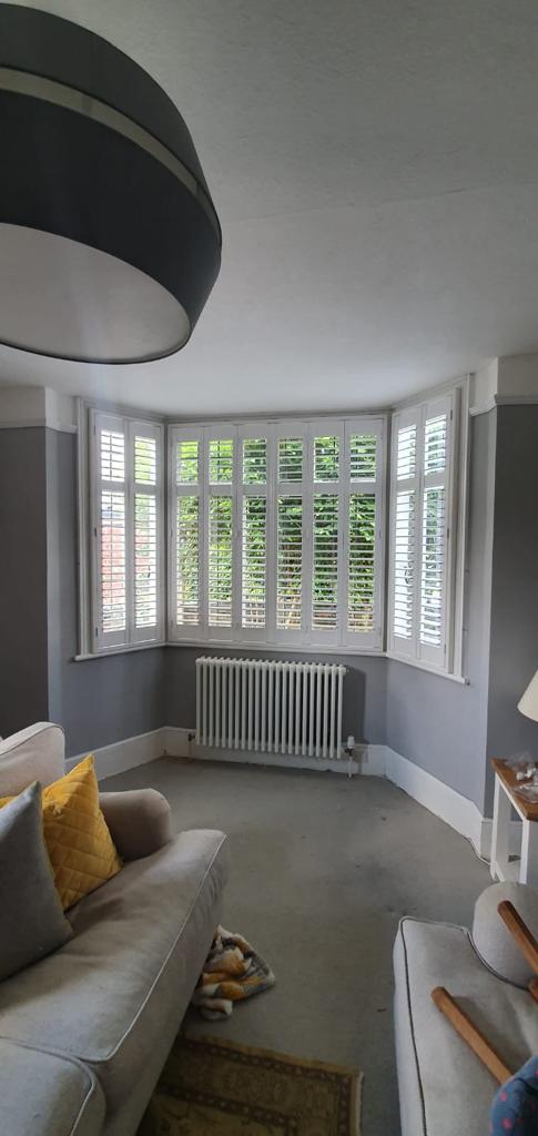 A living room with a couch , lamp , radiator and shutters on the windows.