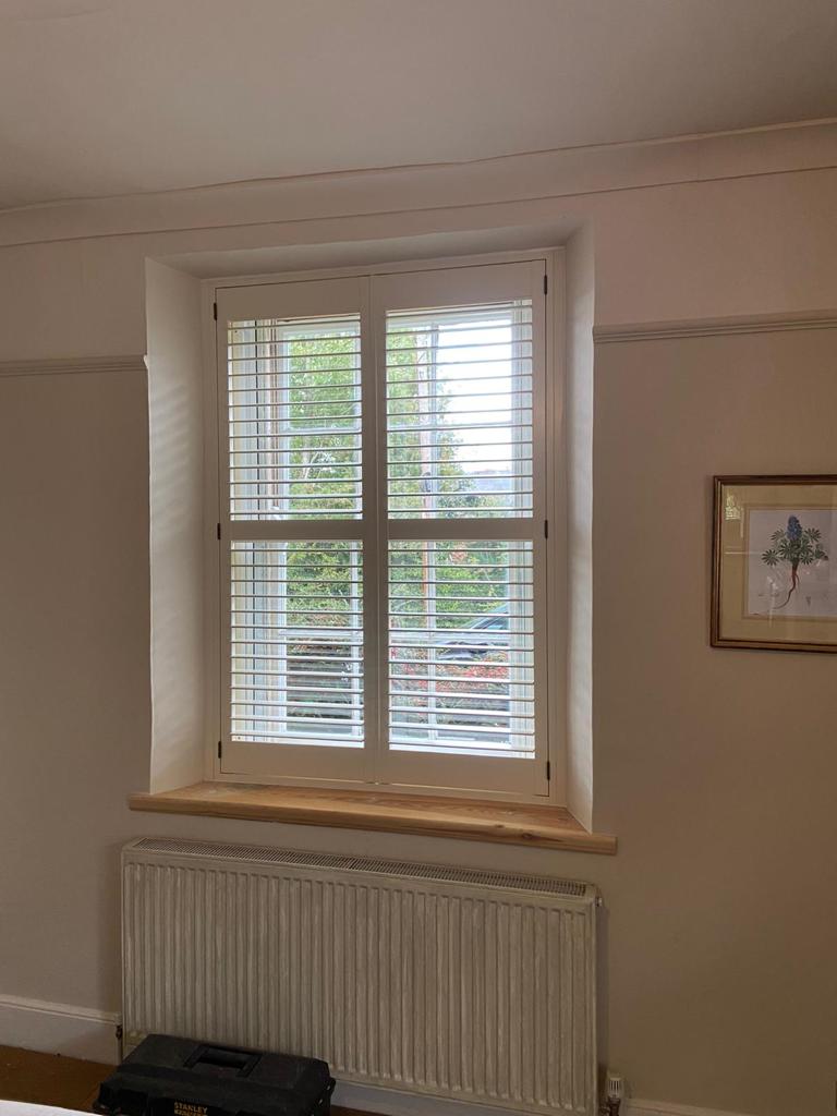 A bedroom with a window with shutters and a radiator.