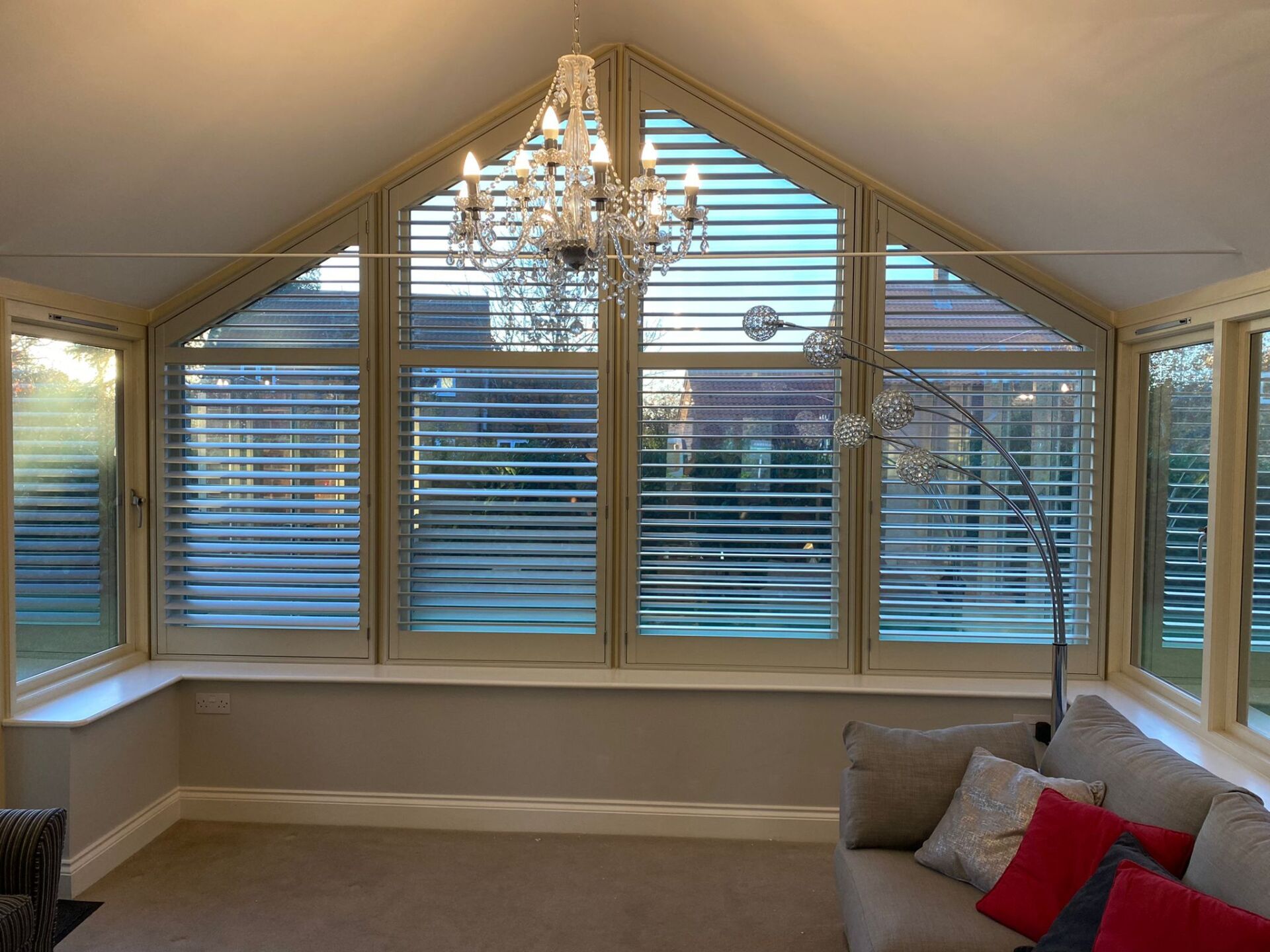 A living room with a couch and a chandelier and shutters on the windows.