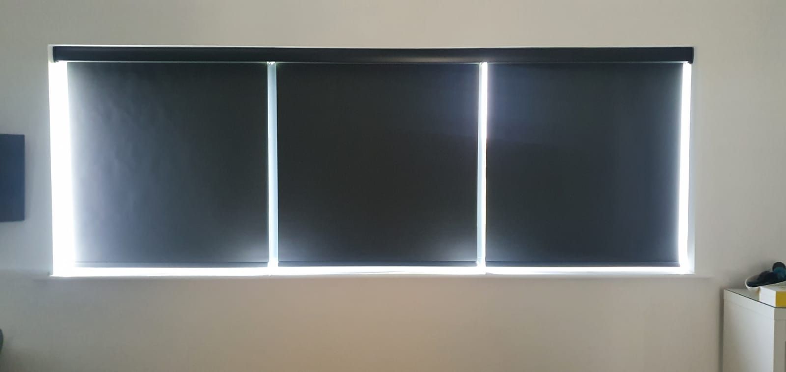 Three black blinds are hanging on a window in a room.